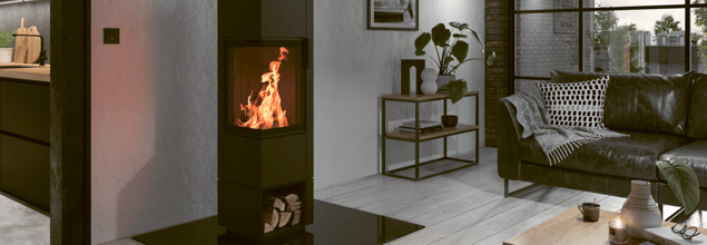 Ein scharzer Piko S steel Kaminofen mit loderndem Feuer steht in einem Wohnzimmer neben einer Couch und einem Beistelltisch.