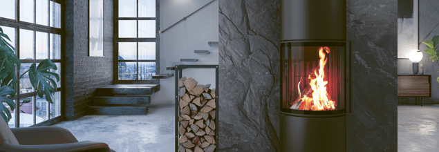 Der Passo L Kaminofen steht vor einer grauen Steinwand neben einem kleinen Holzregal und dient als Raumteiler.