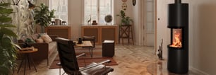 Ein Kaminofen steht an der rechten Wand eines gemütlichen Wohnzimmers neben einem Sessel.
