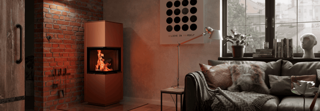 Ein kupferfarbener Kaminofen steht in der Ecke eines Wohnzimmers neben einer Couch und einem Fenster.