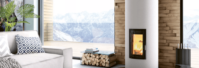 Ein weißer Kaminofen steht vor einem großen Fenster neben einer beigen Couch.